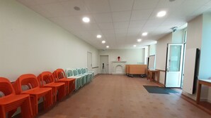 Un salón de conferencias con hileras de sillas anaranjadas, una pizarra, una chimenea y una puerta que da a otra habitación.