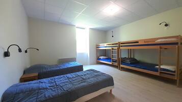Een slaapzaal met twee eenpersoonsbedden en twee stapelbedden, een plafondlamp en een raam met zonwering.