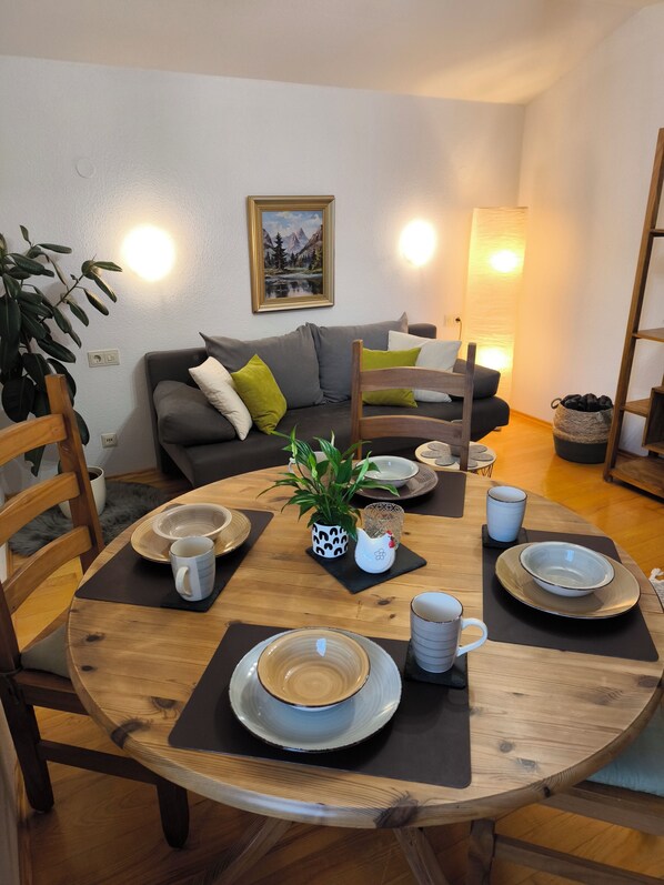 Un coin repas avec une table ronde en bois, dressée pour quatre personnes, entourée de chaises.