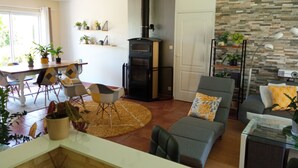 A modern living room with a fireplace, a dining area with chairs and a table, and a kitchen area with a stove. - House surrounded by nature and relaxation for the whole family (Faveraye-Machelles)