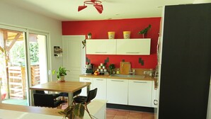 A compact kitchen with white cabinets, a red accent wall, and a dining area with a wooden table and chairs. - House surrounded by nature and relaxation for the whole family (Faveraye-Machelles)