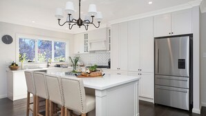 A modern kitchen with white cabinetry, a stainless steel refrigerator, and a chandelier. - Windermere – stunning and garden setting (Burradoo)
