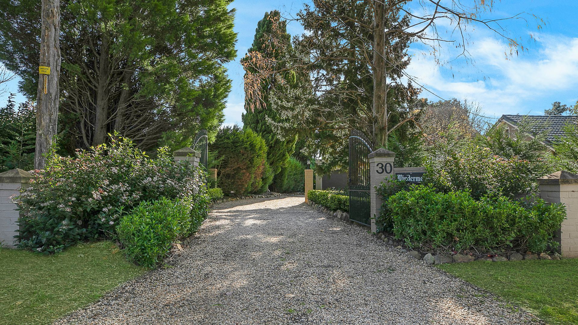 Une allée de gravier mène à une entrée fermée par un portail, sur laquelle est apposée une pancarte indiquant « Piscine privée ».