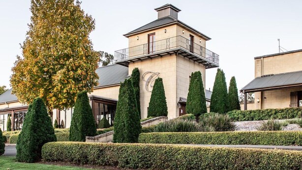A two-story building with a balcony, surrounded by well-manicured hedges and tall trees. - Windermere – stunning and garden setting (Burradoo)