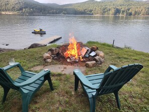 A lakeside campfire with two green Adirondack chairs facing the water. - Gorgeous lake view (Hadley)