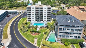 Un hotel de varios pisos con piscina, rodeado de follaje y una carretera curva.