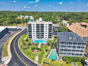 A multi-story hotel with a swimming pool, surrounded by greenery and a curved road. - Cabana One Unit 302 (Myrtle Beach)