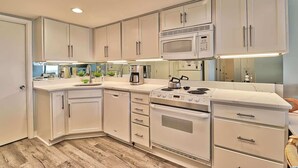Una cocina moderna con armarios blancos, microondas integrado, estufa y lavavajillas.