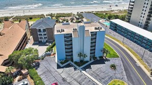 Un hotel de varios pisos con estacionamiento, vista al mar y zona de piscina.