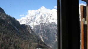 Une vue sur une montagne, avec un sommet enneigé, une forêt dense et un bâtiment situé dans la vallée.