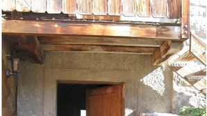 Une porte en bois rustique, dotée d’un loquet en métal, qui donne sur un intérieur faiblement éclairé.