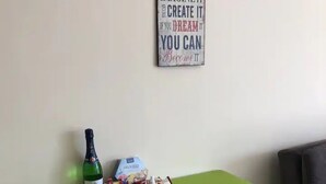 En hyggelig spiseplads med et grønt bord og stole, en vinflaske, snacks og et motiverende citat på væggen.