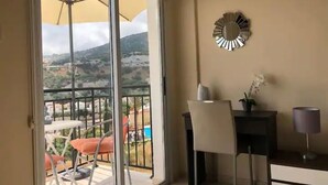 En balkon med udsigt over et bjergrigt landskab, et bord med stole og en dekorativ vægdekoration.
