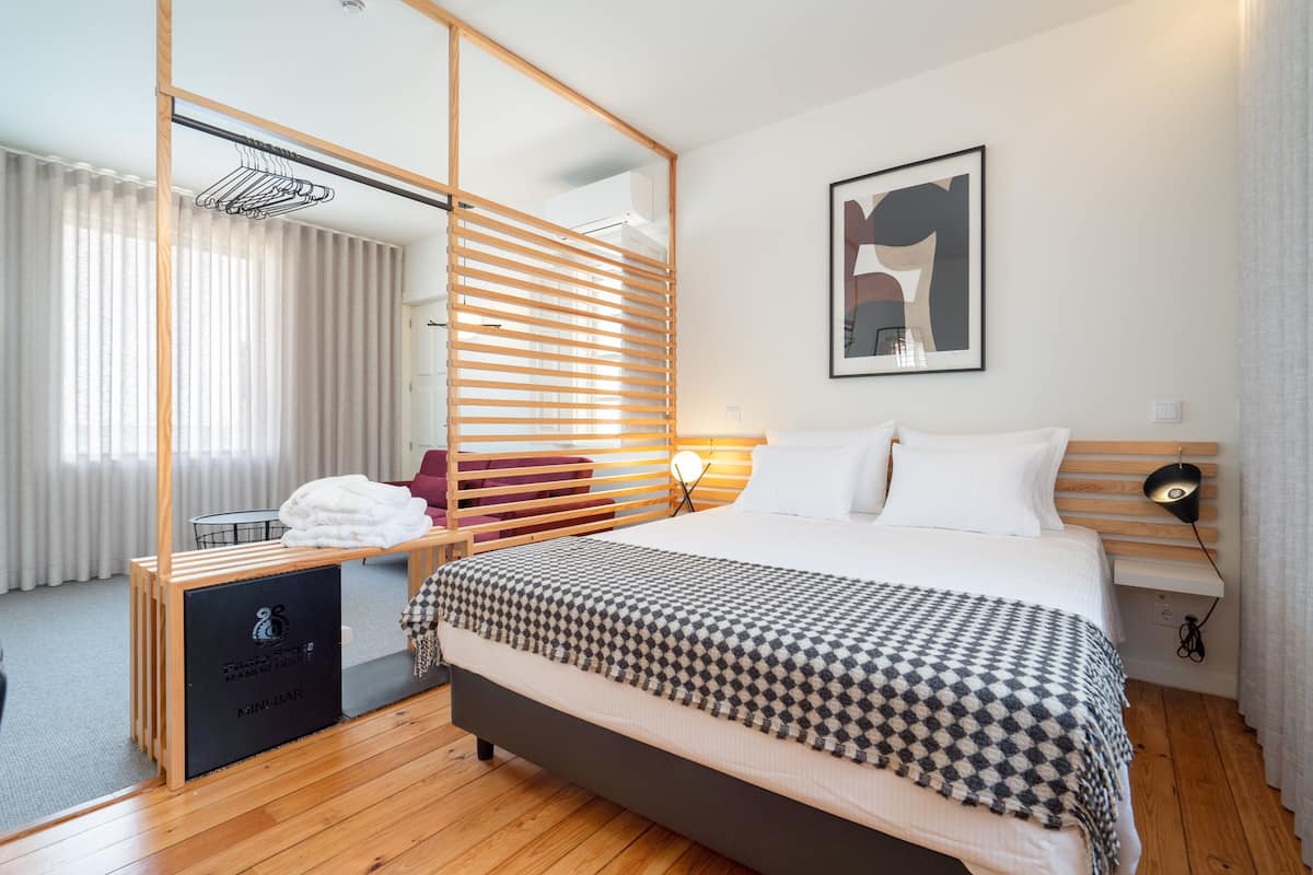 A modern hotel room with a large bed, a wooden desk, a mirror, and a wall-mounted artwork.