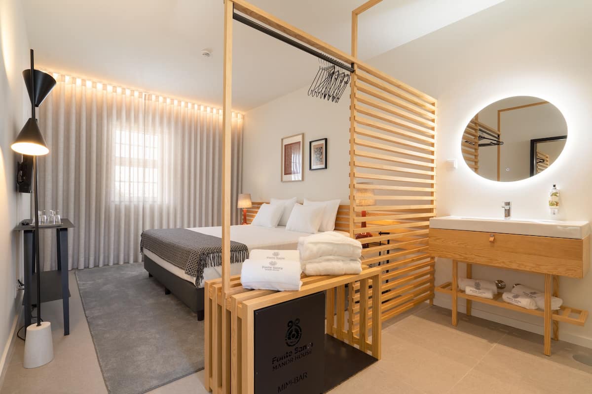 A hotel room with a bed, bedside table, lamp, and a bathroom with a mirror and sink.