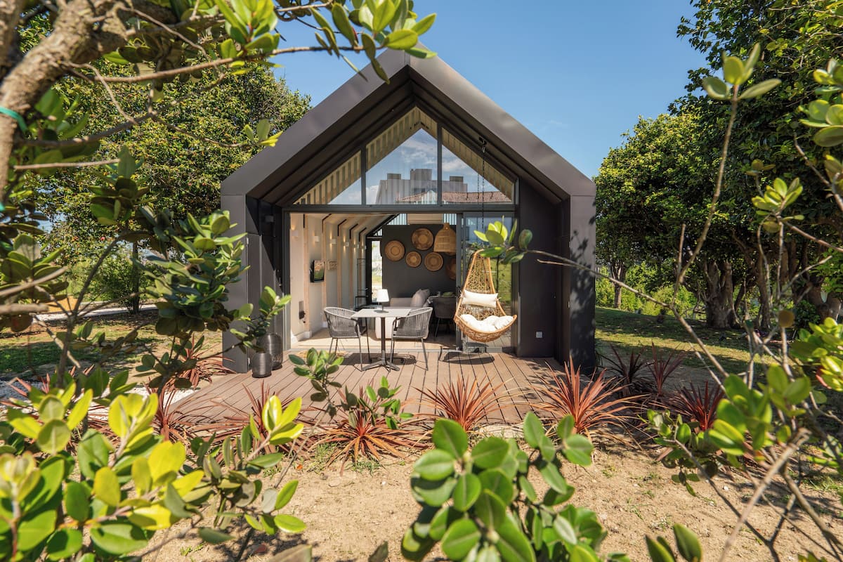 A modern house with a triangular roof, a patio with a table and chairs, and a hanging chair.