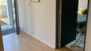 A hallway with a wooden floor, a framed picture on the wall, and a partially open door leading to a room with a bed and a green blanket. - Villa Familiale Centre Bourg sur 2500m² Paysager (Sallebœuf)