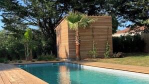 A swimming pool with a wooden deck, surrounded by greenery and a small wooden structure. - Villa Familiale Centre Bourg sur 2500m² Paysager (Sallebœuf)