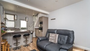 A modern kitchen with a central island, bar stools, and a black leather sofa with a pillow. - Isabel Cottage -  a cottage that sleeps 2 guests  in 1 bedroom (Central Keswick)