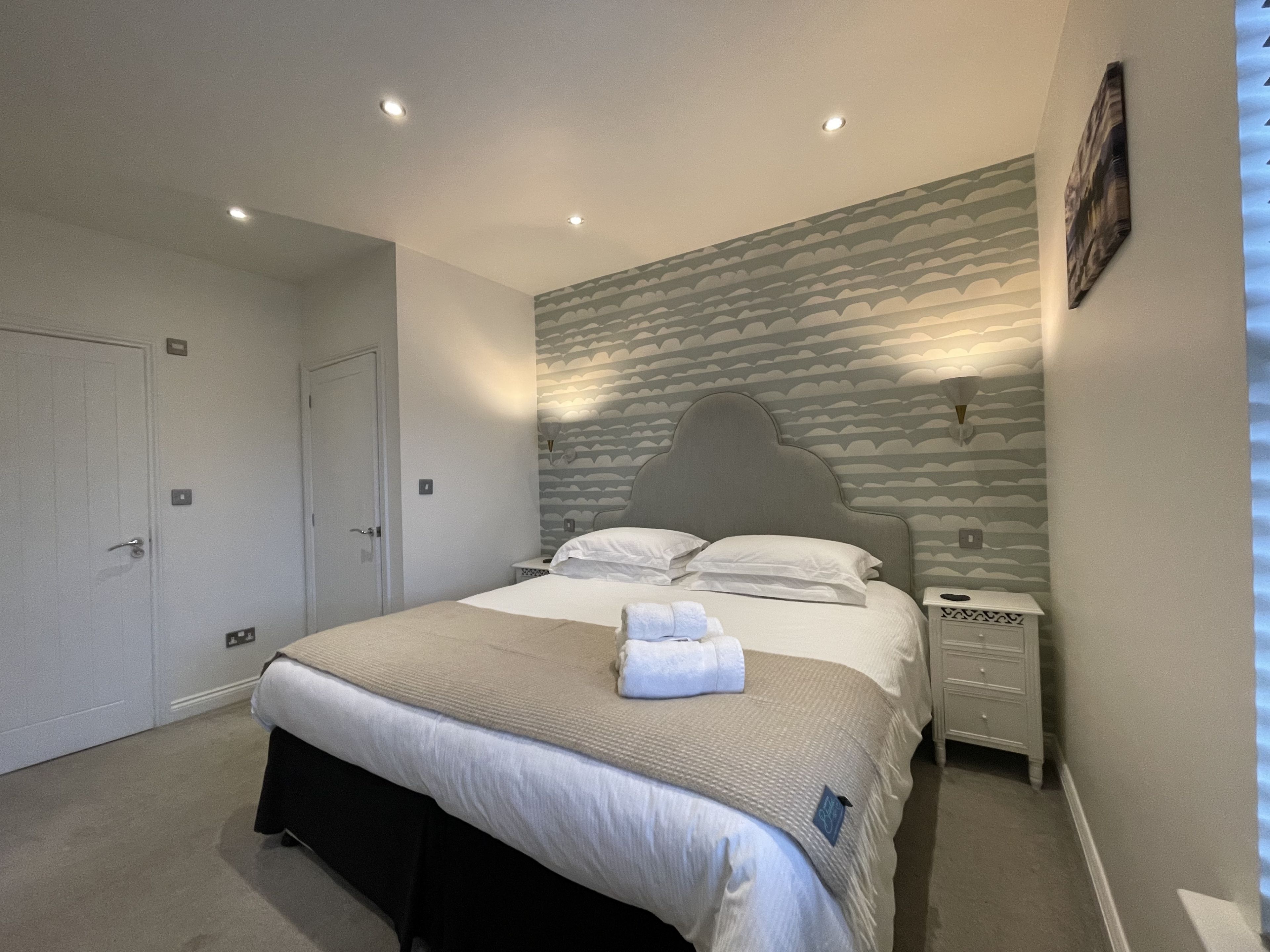 A neatly arranged bedroom with a large bed, bedside tables, a wardrobe, and a patterned wall.