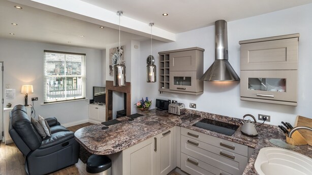 A modern kitchen with a central island, built-in cabinets, and a stainless steel range hood. - Isabel Cottage -  a cottage that sleeps 2 guests  in 1 bedroom (Central Keswick)