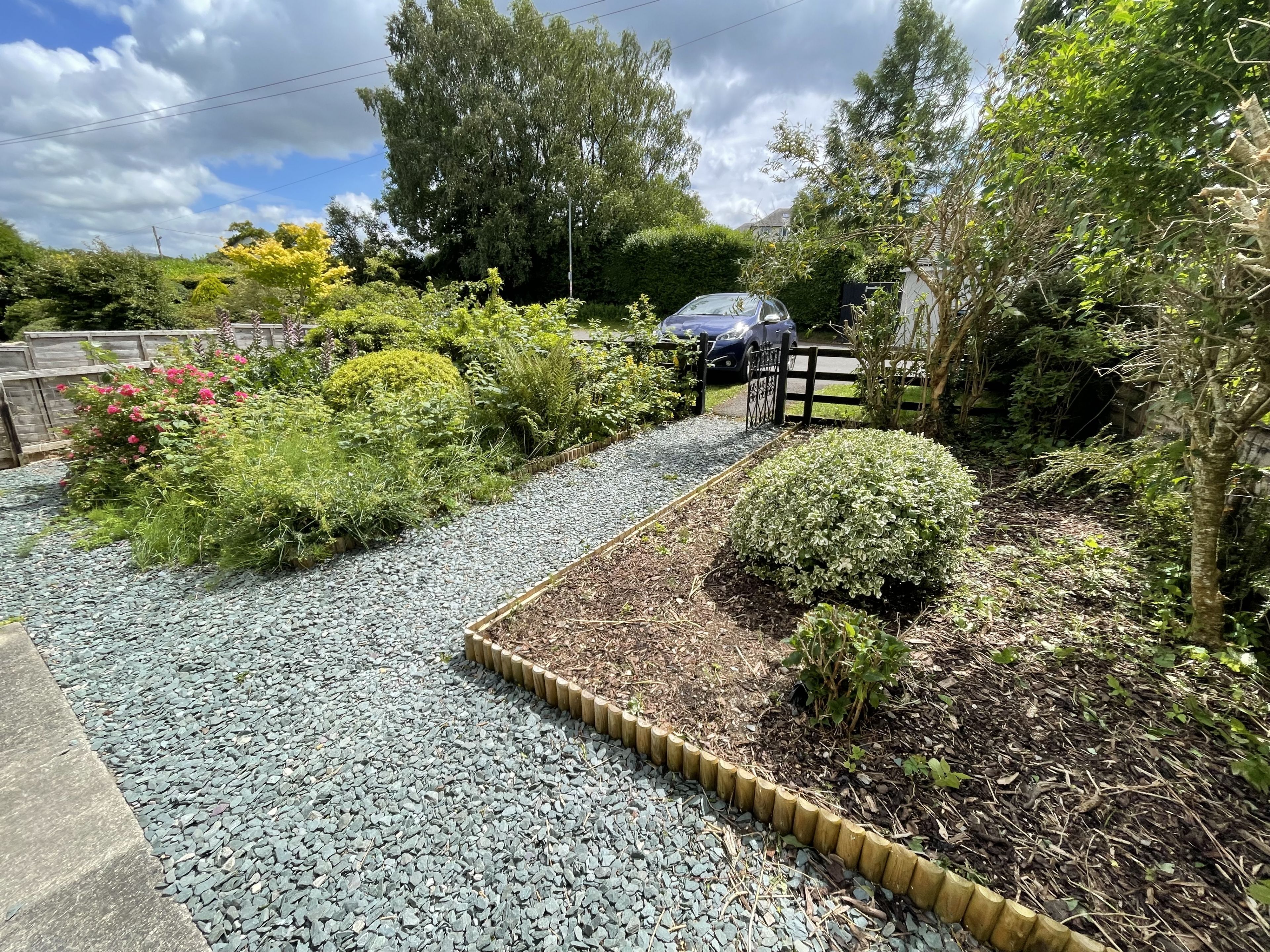 A garden pathway with gravel and mulch, surrounded by various plants and shrubs.