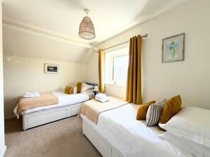 A hotel room with two beds, a window with curtains, a hanging light fixture, and a framed picture on the wall. - Roslin -  a cottage that sleeps 4 guests  in 2 bedrooms (Portinscale)