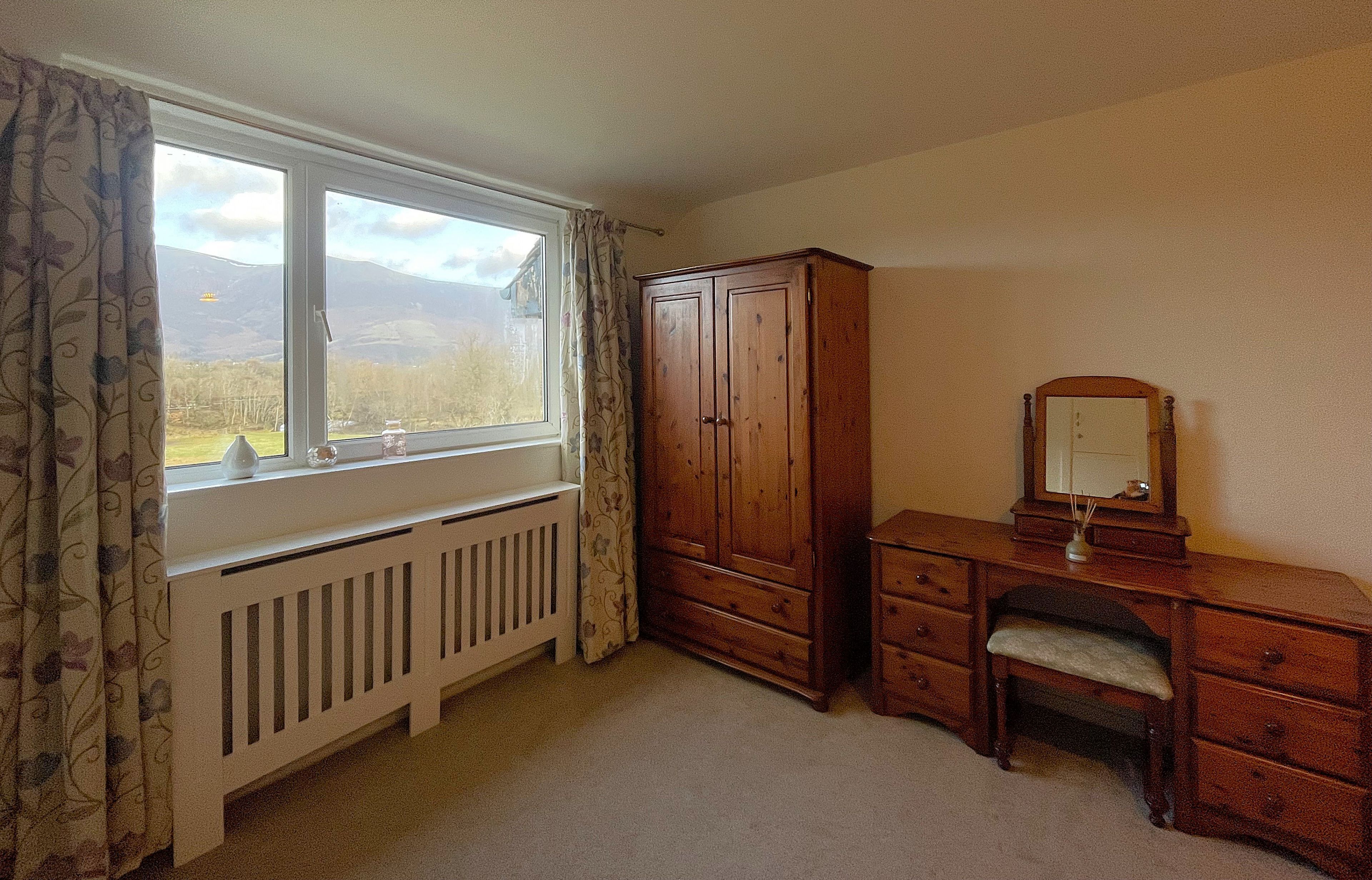 Quarto com uma janela grande, guarda-roupa de madeira, penteadeira com espelho e radiador.