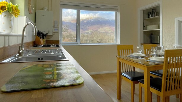 A kitchen with a large window, wooden dining table, and chairs. - Roslin -  a cottage that sleeps 4 guests  in 2 bedrooms (Portinscale)