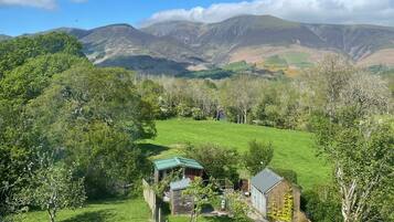 A rural landscape with a small house surrounded by green fields and hills.