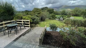 A patio with a table and chairs, surrounded by lush greenery and a view of rolling hills. - Roslin -  a cottage that sleeps 4 guests  in 2 bedrooms (Portinscale)