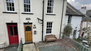 A traditional white building with a red door, a wooden bench outside, and a gravel pathway leading to the entrance.