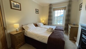 A hotel room with two beds, a dresser, a lamp, a window with curtains, and a painting on the wall.