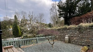 A stone patio with a wooden bench and a squirrel sculpture, surrounded by a stone wall and a wooden fence.