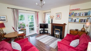 A living room with a fireplace, a television, a bookshelf, and a dining area with a table and chairs. - Greta Bank -  an apartment that sleeps 4 guests  in 2 bedrooms (Central Keswick)