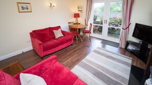 A living room with a red sofa, a TV, and a dining area with a table and chairs. - Greta Bank -  an apartment that sleeps 4 guests  in 2 bedrooms (Central Keswick)