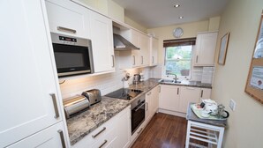 A compact kitchen with white cabinets, a built-in oven, a microwave, and a stainless steel toaster. - Greta Bank -  an apartment that sleeps 4 guests  in 2 bedrooms (Central Keswick)