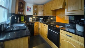 A modern kitchen with wooden cabinets, a black countertop, and stainless steel appliances. - Byways -  a cottage that sleeps 4 guests  in 2 bedrooms (Central Keswick)