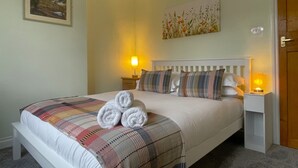 A neatly made bed with a plaid blanket, two bedside lamps, and a painting on the wall. - Byways -  a cottage that sleeps 4 guests  in 2 bedrooms (Central Keswick)