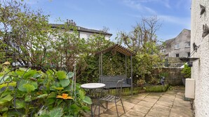 A patio with a table and chairs, surrounded by greenery and a pergola. - Byways -  a cottage that sleeps 4 guests  in 2 bedrooms (Central Keswick)