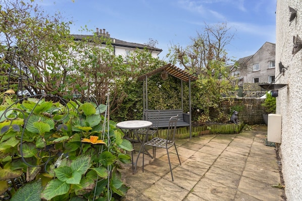 A patio with a table and chairs, surrounded by greenery and a pergola.