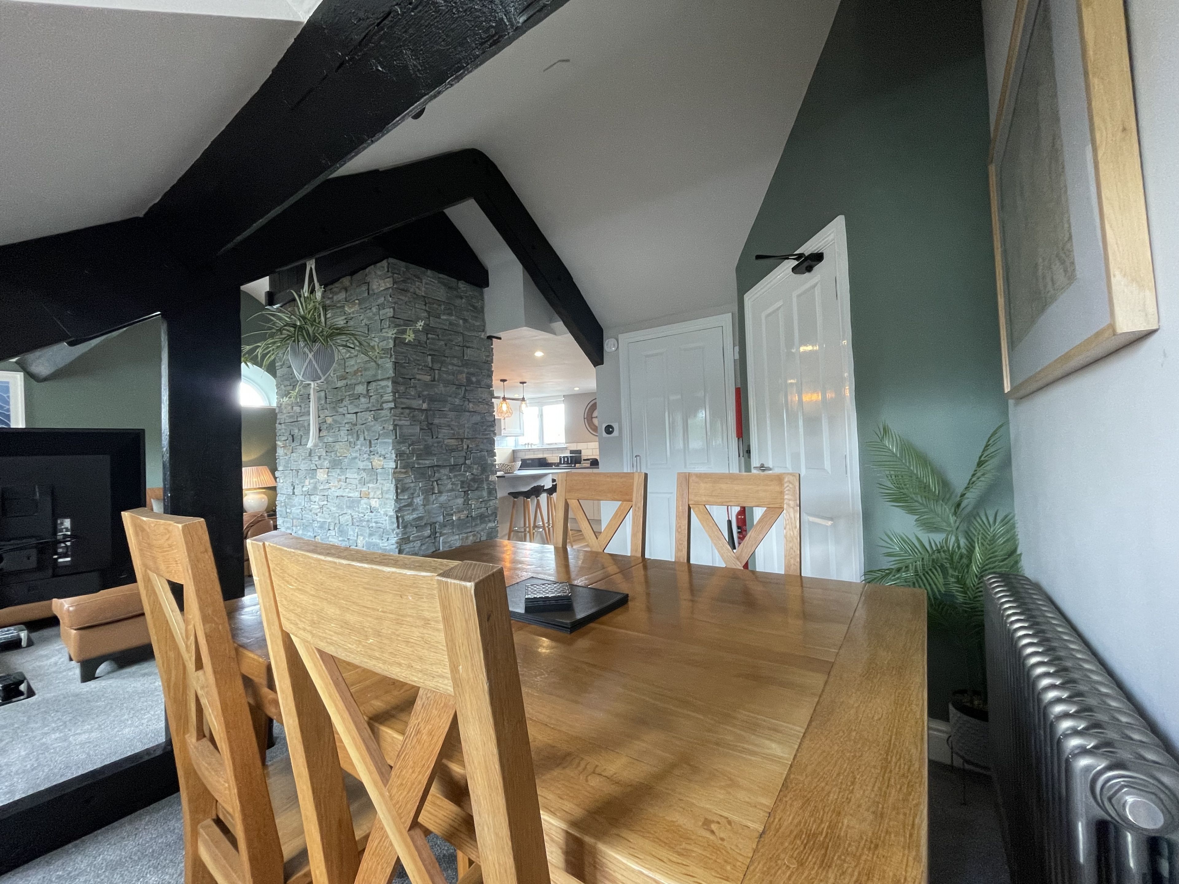 Un comedor con mesa y sillas de madera, un pilar de piedra y vista a la cocina.