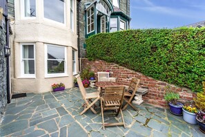 Eine Terrasse mit Steinboden, Holzmöbeln und Topfpflanzen.