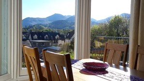 Un balcón con mesa y sillas, con vista a una zona residencial con casas y montañas.