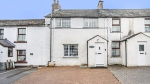 A white two-story building with a brick driveway and a small front garden. - Millside Cottage -  a cottage that sleeps 4 guests  in 2 bedrooms (Braithwaite)