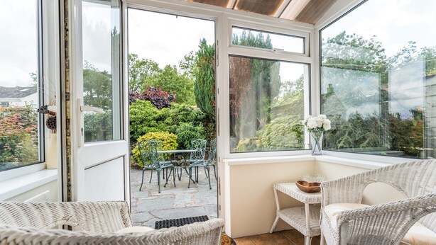 A conservatory with wicker furniture, a stone floor, and a view of a garden. - Millside Cottage -  a cottage that sleeps 4 guests  in 2 bedrooms (Braithwaite)