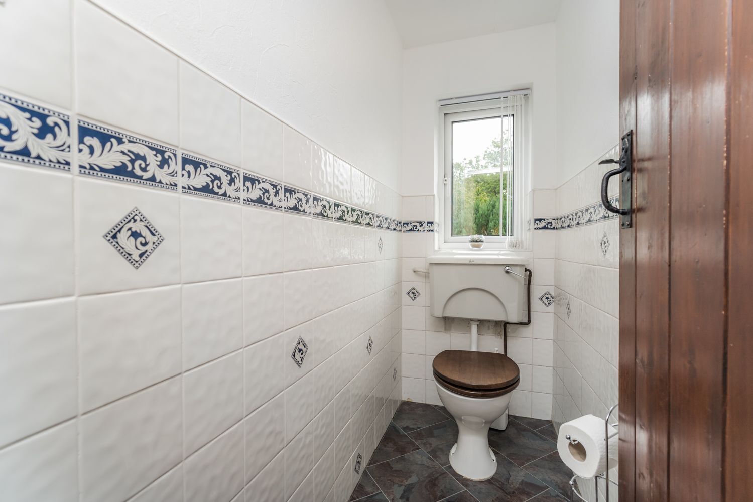 Ein kleines Badezimmer mit weißen Fliesen, einer Toilette und einem Fenster.