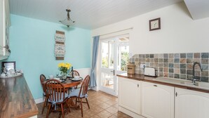 A kitchen with a dining area, featuring a wooden table and chairs, a tiled backsplash, and a window with curtains. - Millside Cottage -  a cottage that sleeps 4 guests  in 2 bedrooms (Braithwaite)