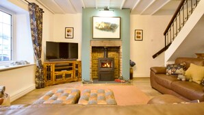 A living room with a fireplace, a television, a sofa, and a staircase. - Millside Cottage -  a cottage that sleeps 4 guests  in 2 bedrooms (Braithwaite)