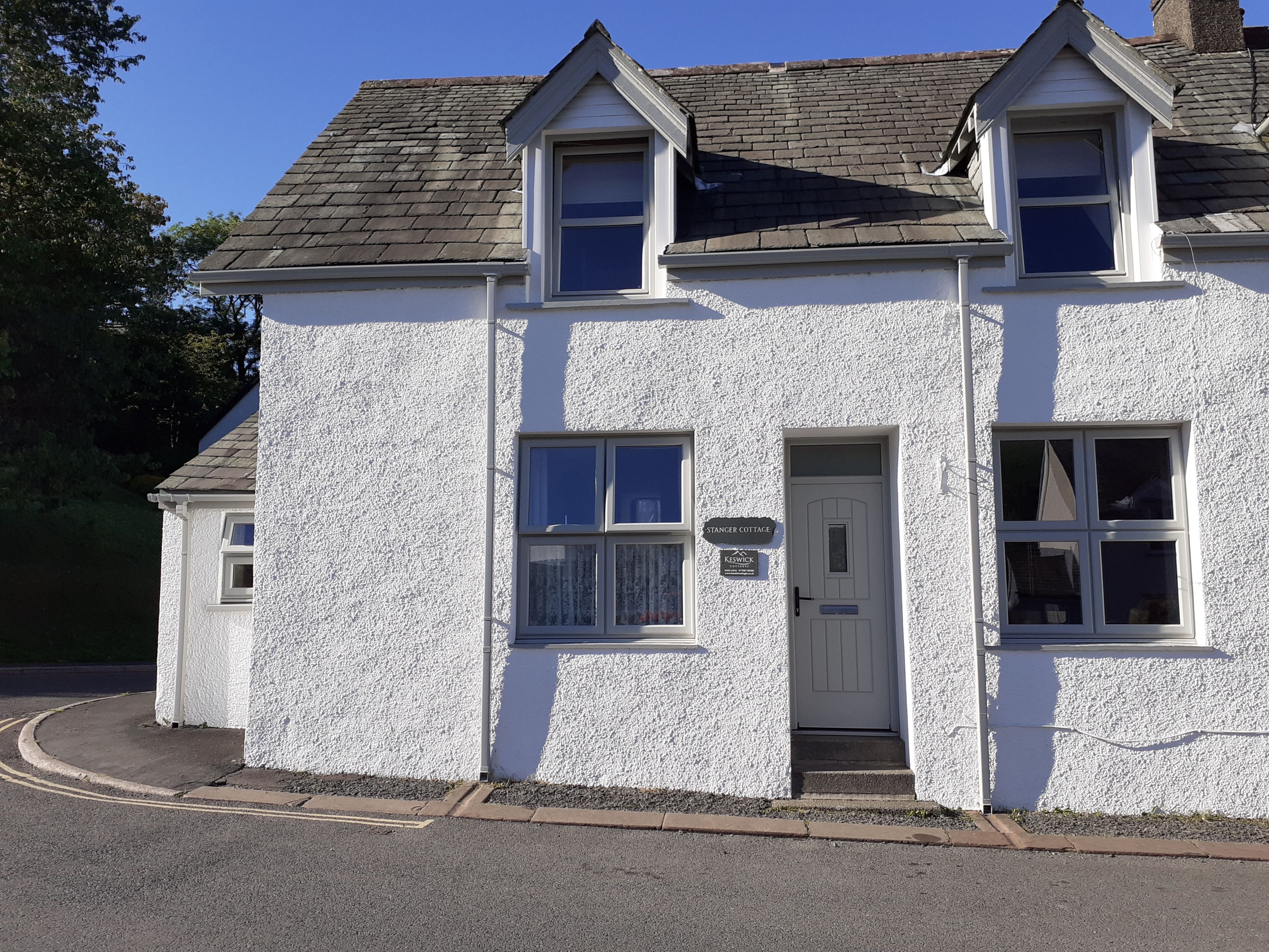 Une maison de campagne à deux étages, avec une façade blanche, une porte d’entrée et deux fenêtres à l’étage supérieur.